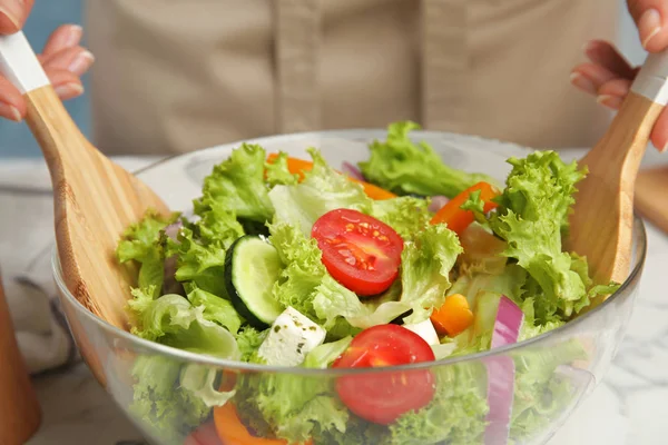 Mulher preparando saborosa salada grega fresca na tigela à mesa, close-up — Fotografia de Stock