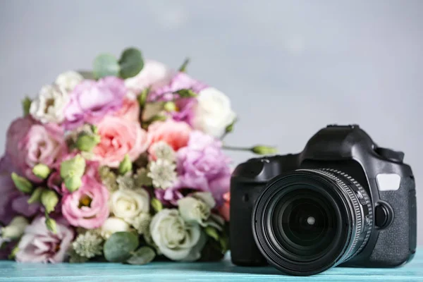 Modern camera and bouquet on light blue wooden table. International Photographer\'s day