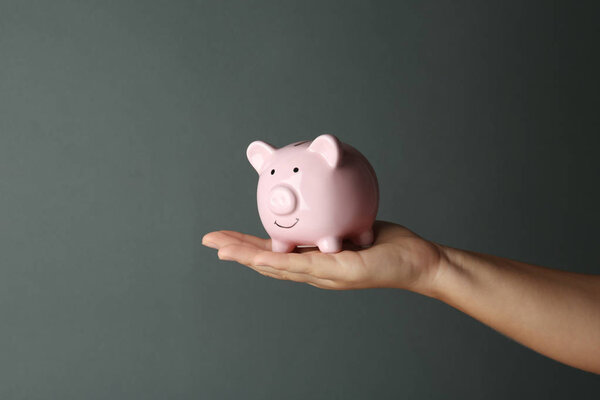 Woman holding piggy bank on dark grey background, closeup view