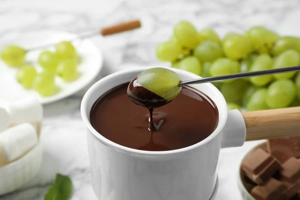 Weintrauben in Fonduetopf mit dunkler Schokolade auf Marmortisch tauchen — Stockfoto