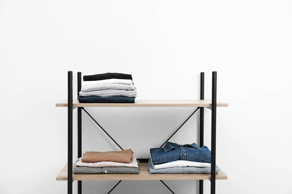 Modern shelves unit with stacked clothes near white wall — Stock Photo, Image