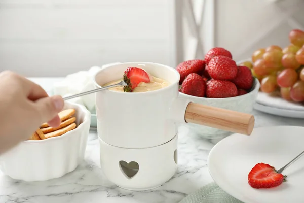 Woman dipping strawberry into fondue pot with white chocolate at marble table — Stok fotoğraf