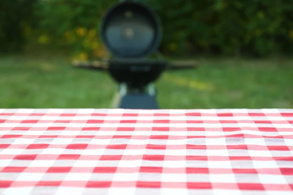 Picnic table with cloth against blurred barbecue grill outdoors