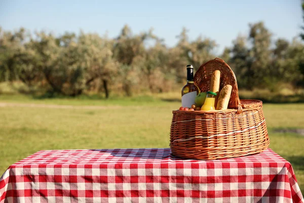 Cesta de piquenique de vime com vinho e lanches na mesa no parque. Espaço para texto — Fotografia de Stock