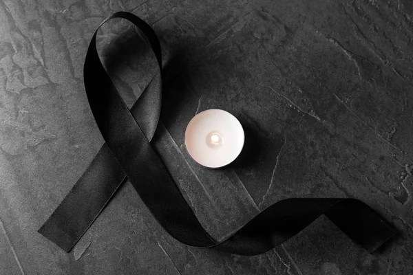 Black ribbon and burning candle on dark grey stone surface, top view. Funeral symbols — Stock Photo, Image