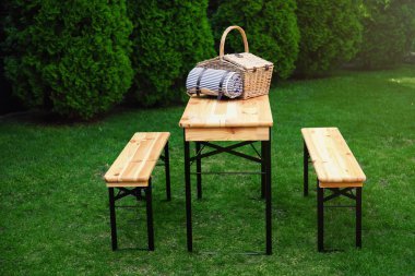 Parkta ahşap masa üzerinde battaniye ile Hasır piknik sepeti