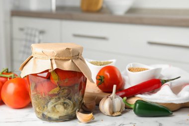 Cam kavanozda domates turşusu ve mutfakta beyaz mermer masada ürünler