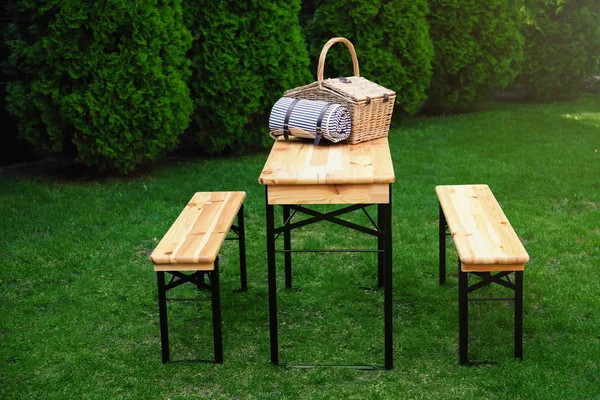 Parkta ahşap masa üzerinde battaniye ile Hasır piknik sepeti