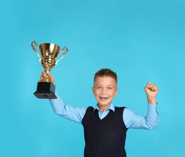 Happy boy in school uniform met gouden winnende Cup op blauwe achtergrond — Stockfoto
