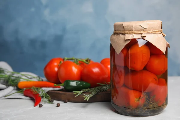 Jar with pickled tomatoes and vegetables on grey table against blue background — Stock Photo, Image