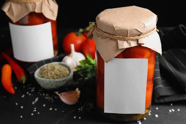Frascos de tomates en escabeche con pegatinas en blanco y productos en mesa negra —  Fotos de Stock