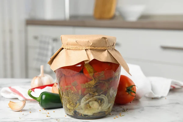 Tomates en vinagre en frasco de vidrio y productos en mesa de mármol blanco en la cocina — Foto de Stock