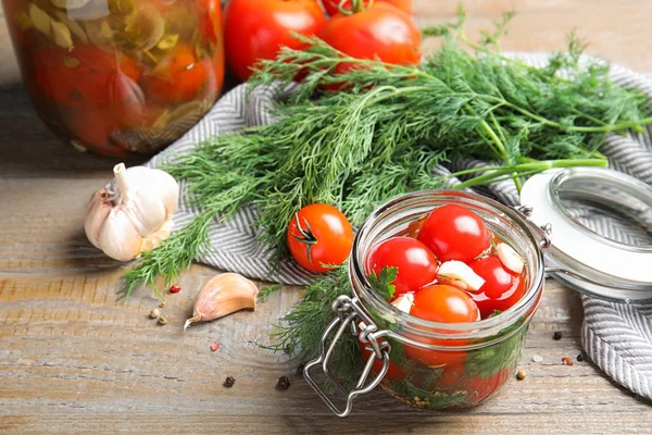 Gepekelde tomaten in glazen potten en producten op houten tafel — Stockfoto