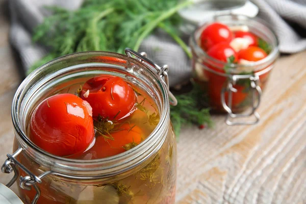 Pickled tomatoes in glass jars and products on wooden table, closeup view — Stock Photo, Image