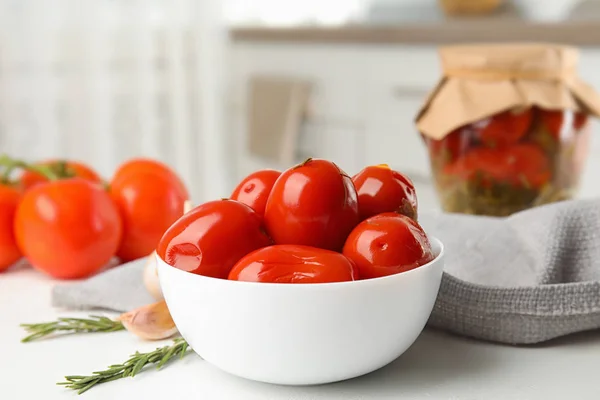 Gepekelde tomaten in de kom in de buurt van glazen pot op witte keuken tafel — Stockfoto