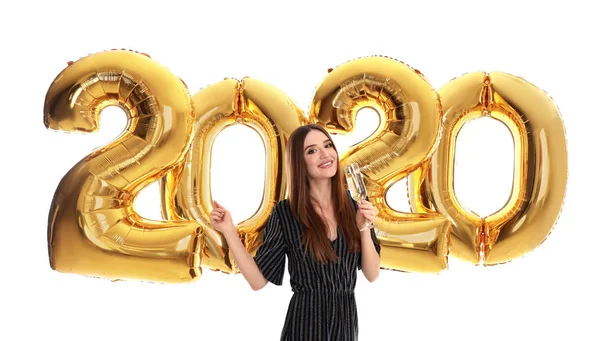 Giovane donna felice con un bicchiere di champagne vicino palloncini dorati 2020 su sfondo bianco. Festeggiamenti di Capodanno — Foto Stock