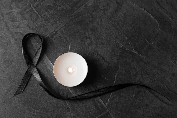 Black ribbon and burning candle on dark grey stone surface, top view. Funeral symbols — Stock Photo, Image