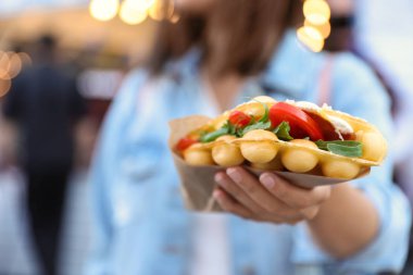Genç kadın domates ve arugula açık havada lezzetli kabarcık waffle tutan, closeup