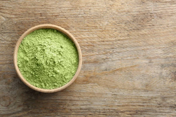 Bowl of wheat grass powder on wooden table, top view. Space for text