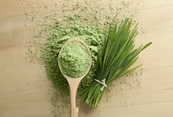 Spoon of wheat grass powder and green sprouts on wooden table, flat lay