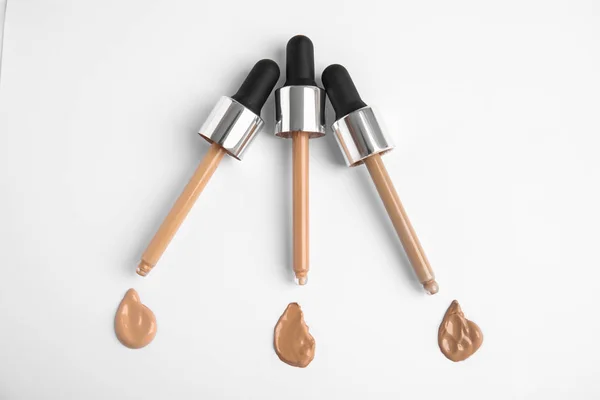 Samples of different foundation shades and droppers on white background, top view