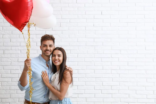 Casal jovem com balões de ar perto da parede de tijolo branco. Celebração do Dia de São Valentim — Fotografia de Stock