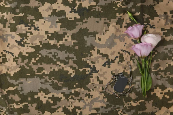 Flores frescas y etiqueta de identificación sobre fondo de camuflaje, disposición plana con espacio para el texto. Día de las Fuerzas Armadas — Foto de Stock