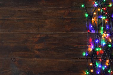 Kahverengi ahşap arka plan üzerinde Parlayan Noel ışıkları, üst görünümü. Metin için alan