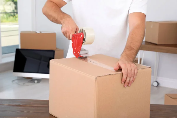 Young worker packing cardboard box in room, closeup. Moving service — Stock Photo, Image