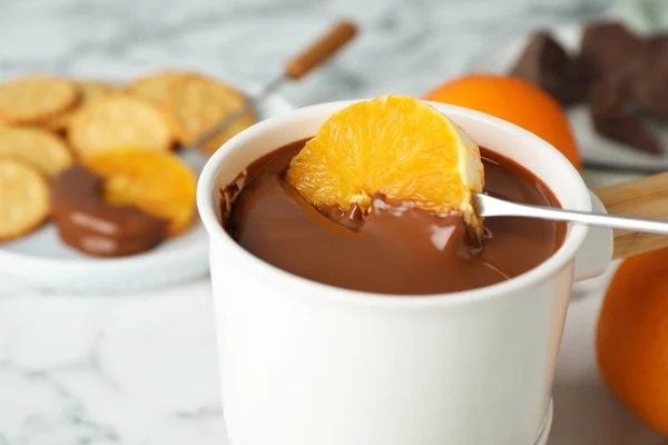 Orange in Fonduetopf mit Schokolade auf weißem Marmortisch tauchen, Nahaufnahme — Stockfoto