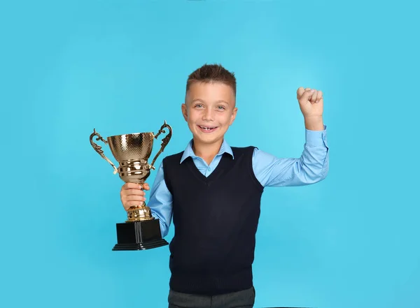 Happy boy in school uniform met gouden winnende Cup op blauwe achtergrond. Ruimte voor tekst — Stockfoto