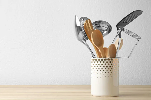 Set de utensilios de cocina en pie sobre mesa de madera cerca de pared de luz. Espacio para texto — Foto de Stock