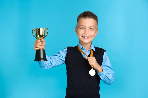 Happy boy in school uniform met gouden winnende Cup en medaille op blauwe achtergrond — Stockfoto