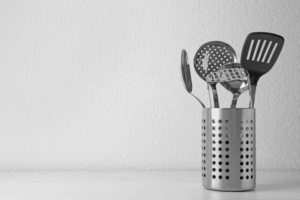 Set de utensilios de cocina en pie sobre mesa de madera cerca de pared de luz. Espacio para texto — Foto de Stock