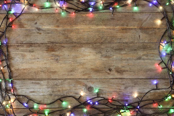 Rám zářících vánočních světel na dřevěném pozadí, pohled shora. Místo pro text — Stock fotografie