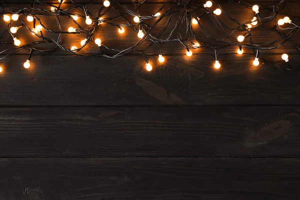 Leuchtende Weihnachtsbeleuchtung auf dunklem Holzhintergrund, Draufsicht. Raum für Text — Stockfoto