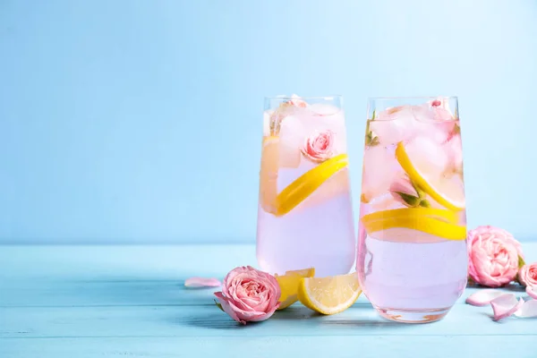 Tasty refreshing lemon drink with roses on wooden table against light blue background. Space for text — Stock Photo, Image