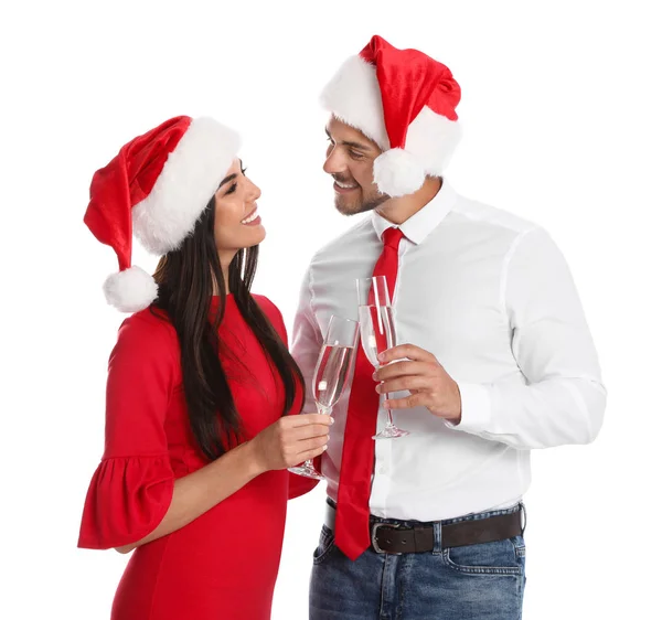 Casal jovem encantador em chapéus de Papai Noel com copos de champanhe no fundo branco. Celebração de Natal — Fotografia de Stock
