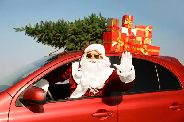 Autêntico Papai Noel com presentes e abeto no telhado dirigindo carro moderno ao ar livre — Fotografia de Stock