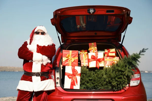 Autêntico Papai Noel perto de carro com tronco aberto cheio de presentes e abeto ao ar livre — Fotografia de Stock
