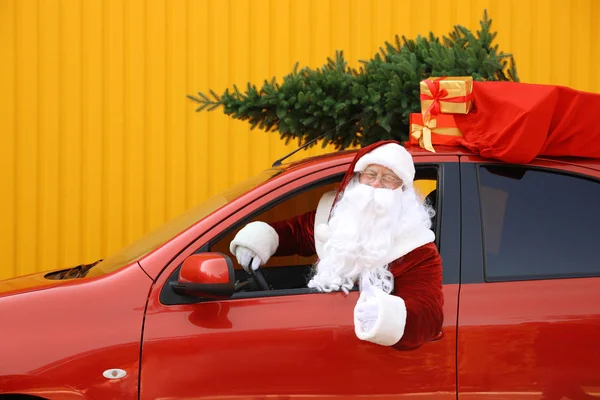 Autentico Babbo Natale con abete e borsa piena di regali guida auto contro sfondo giallo — Foto Stock