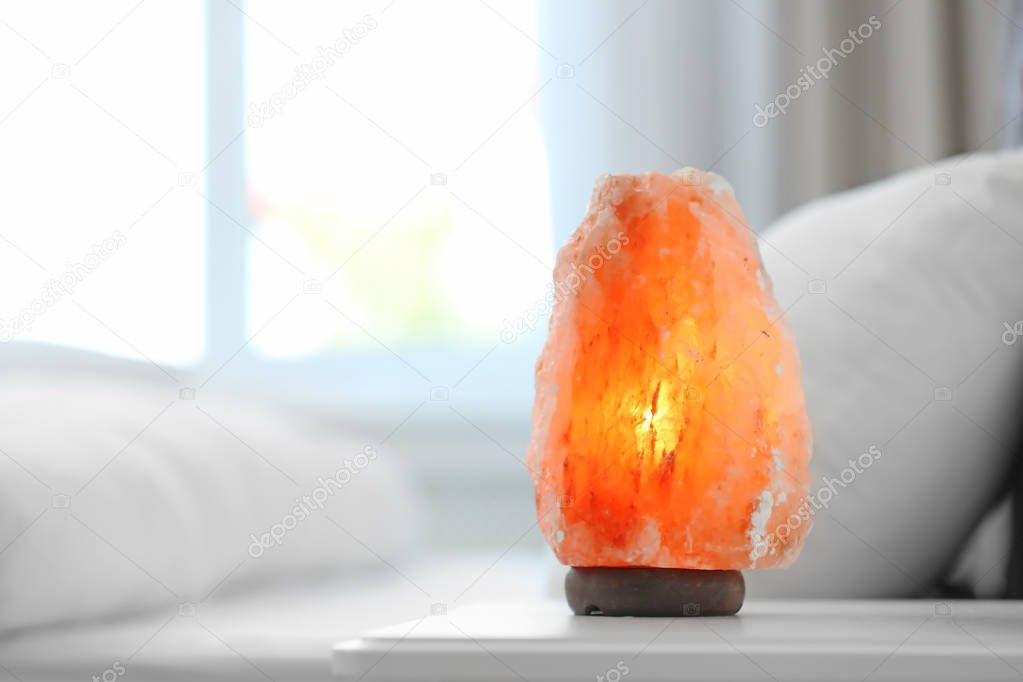 Himalayan salt lamp on table in bedroom. Space for text