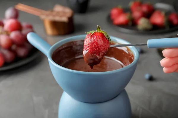 Femme trempant fraise dans un pot avec fondue au chocolat à table, gros plan — Photo