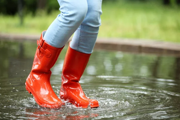 赤いゴムのブーツを持つ女性が水たまりに飛び込み、クローズアップ。雨天 — ストック写真