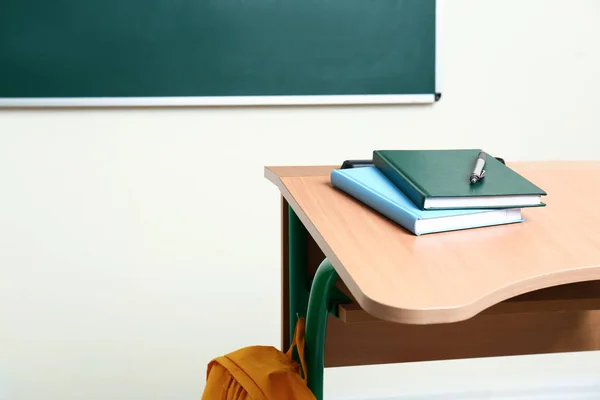 Bureau scolaire en bois avec papeterie près du tableau en salle de classe — Photo