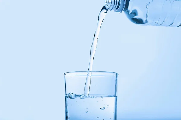 Nalewanie wody z butelki do szklanki na niebieskim tle. Orzeźwiający napój — Zdjęcie stockowe