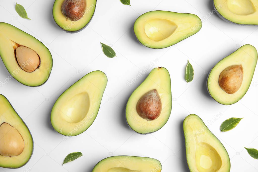 Cut fresh ripe avocados and leaves on white background, top view