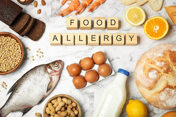 Flat lay composition of different products and wooden cubes with words Food Allergy on white marble table — Stock Photo, Image