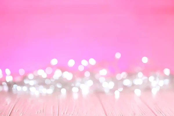White Christmas lights on pink wooden table, blurred view — Stock Photo, Image