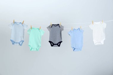 Açık gri arka plan karşı giysi hattı üzerinde asılı farklı bebek onesies. Çamaşır günü